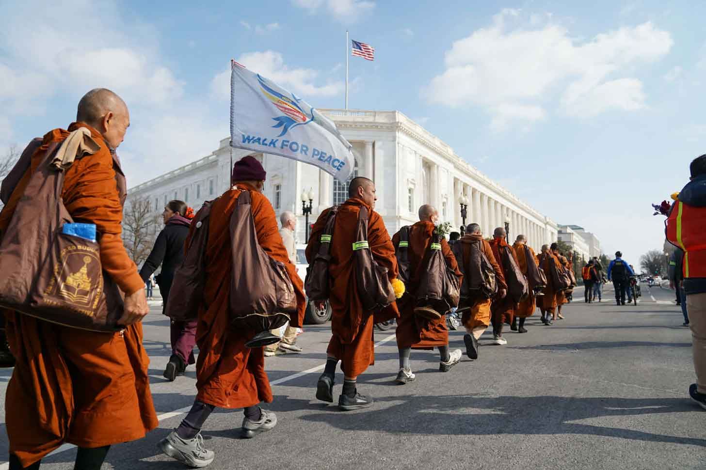 A group of 19 Buddhist monks in orange robes walk along the National Mall in Washington, D.C.