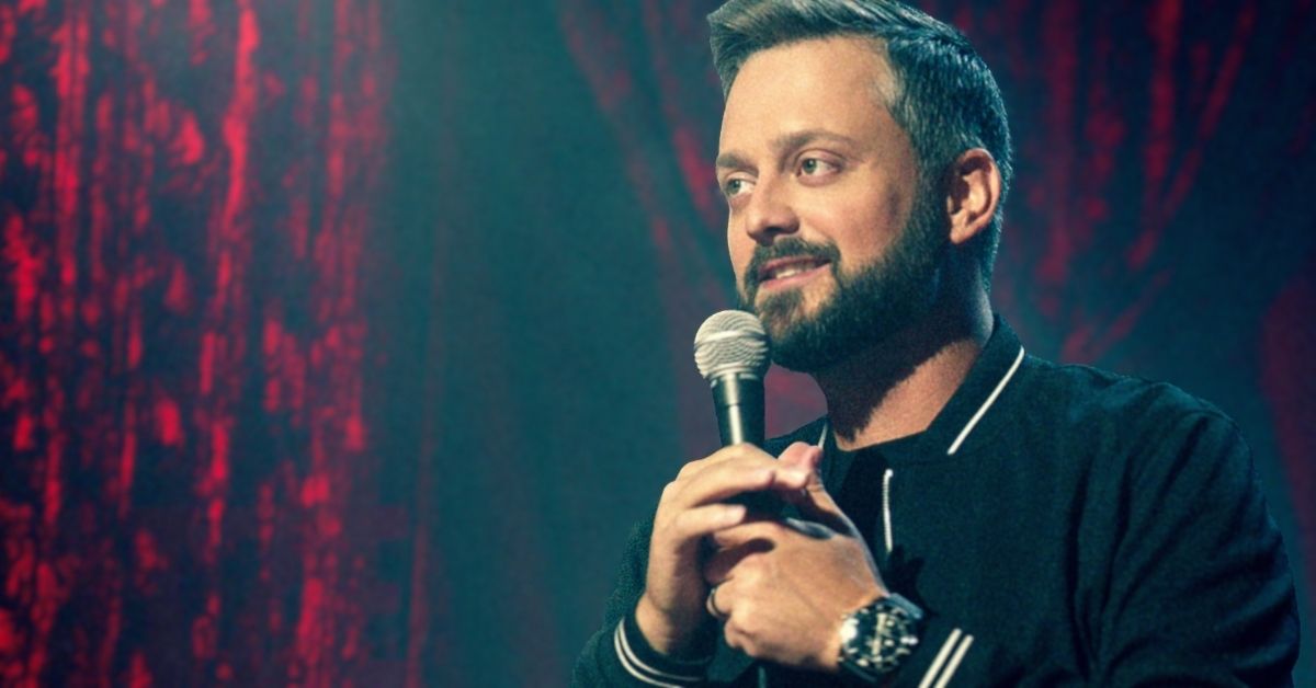 Nate Bergatze smiles as he holds a microphone by a red curtain in a promotional still for the stand-up special "The Tennessee Kid."