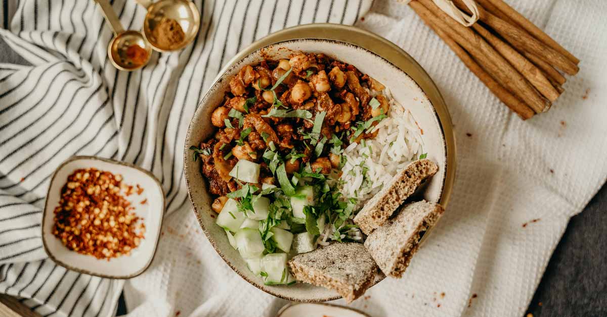An aerial view of a dish of chickpeas, rice, vegetables, and pita bread on a table