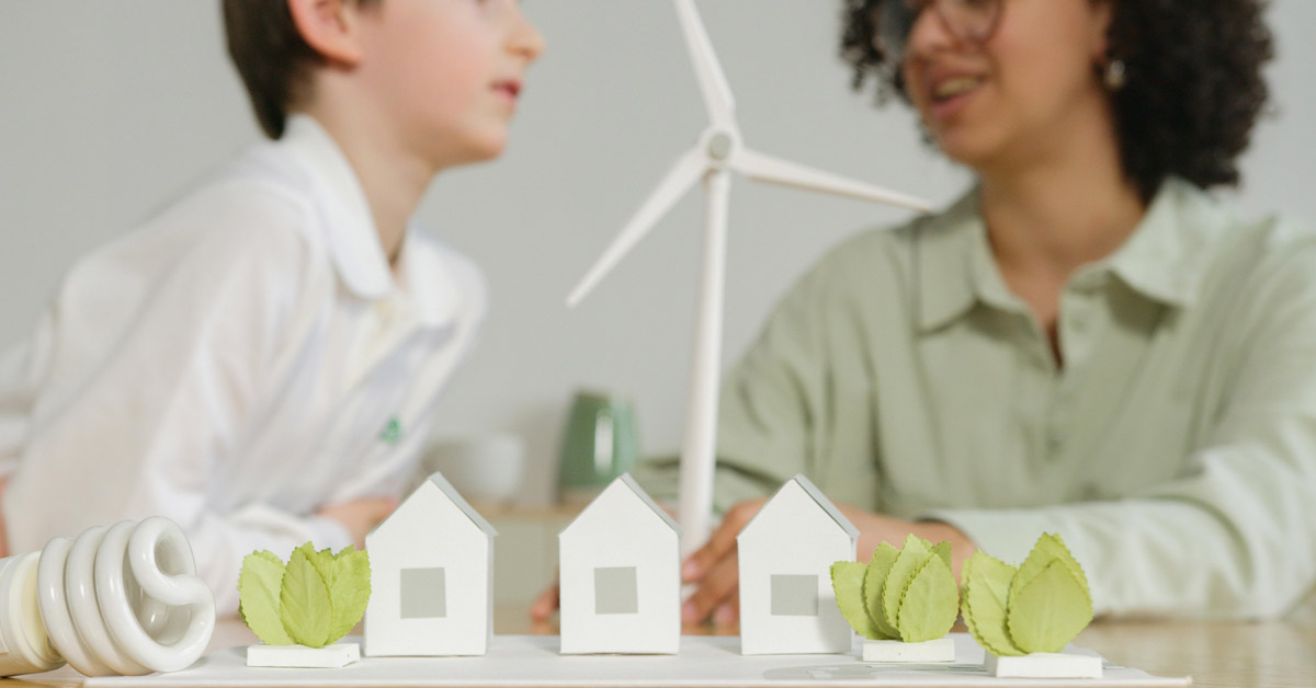 Two students converse next to a 3D model of a wind turbine, trees, and houses