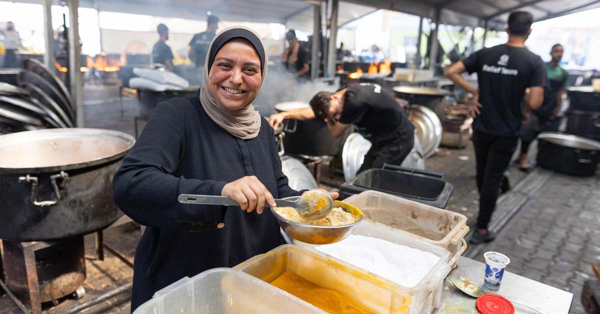 A woman in a hijab smiles while serving a hot bowl of food in Gaza for World Central Kitchen