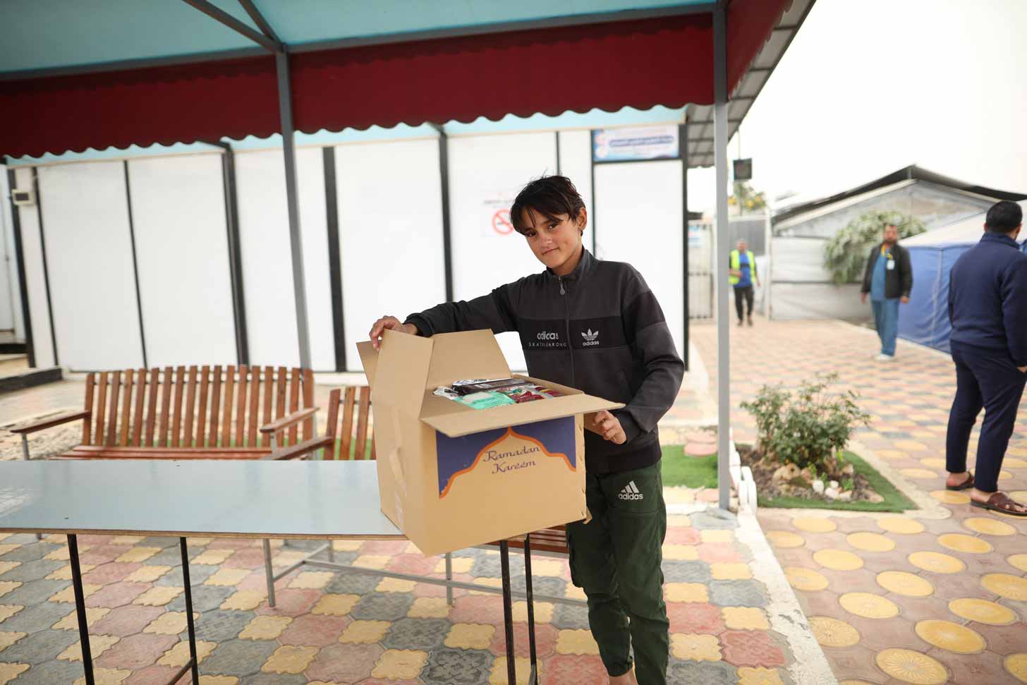 A young boy in Gaza holds a large cardboard box filled with food for Ramadan 