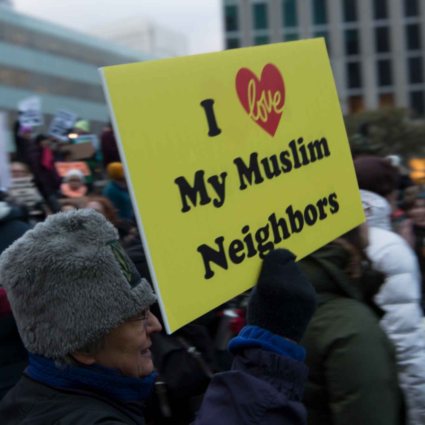 An older man walks through a protest crowd with a yellow sign that says "I LOVE MY MUSLIM NEIGHBORS"