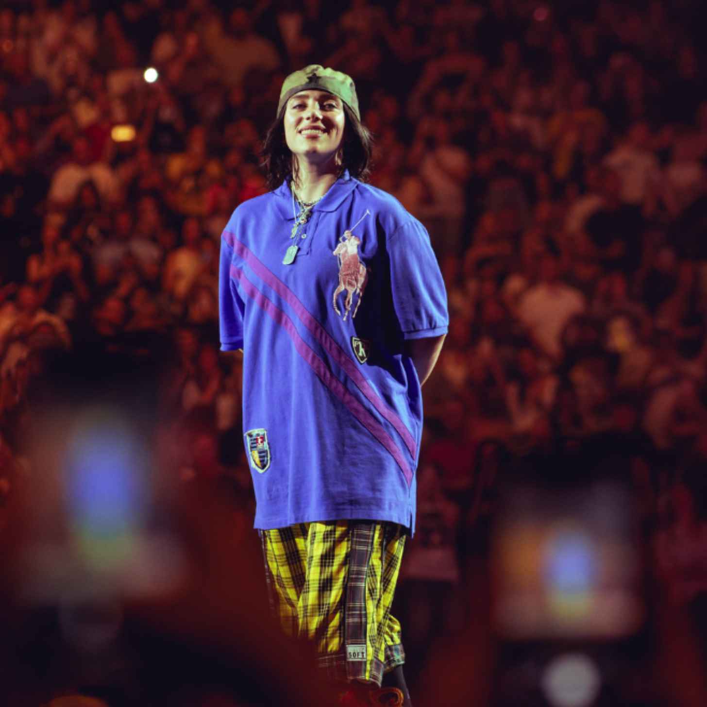 Billie Eilish stands on stage smiling at a concert. 