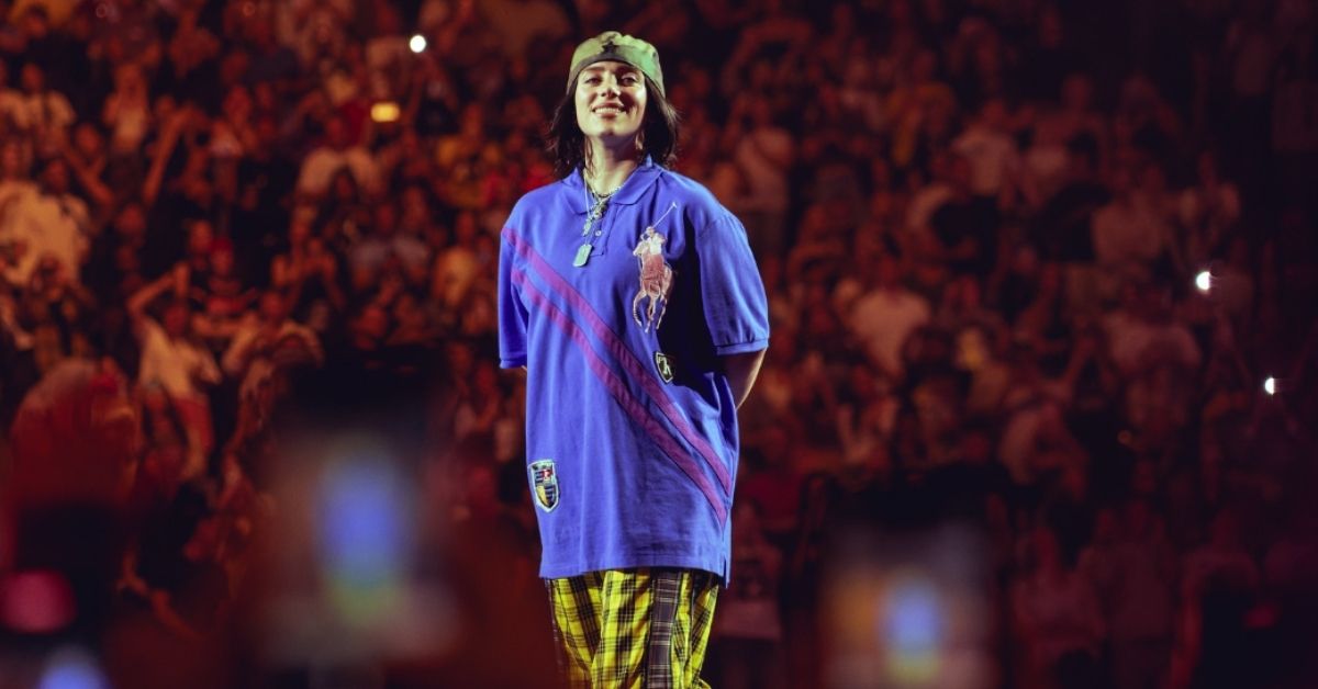 Billie Eilish stands on stage smiling at a concert. 