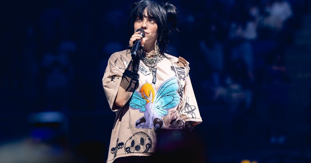 Billie Eilish stands center stage during a concert tour in 2022. She has black hair put up in two tight buns.
