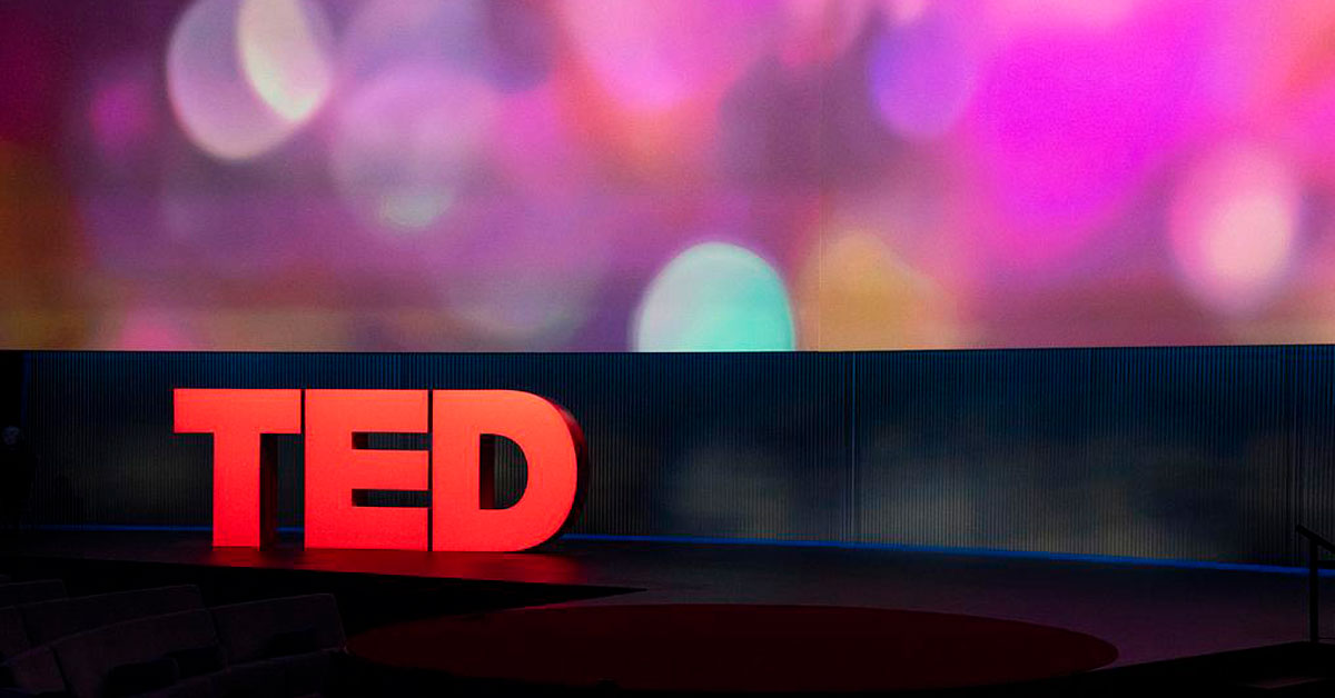 Red TED letters on stage in front of a purple bokeh background