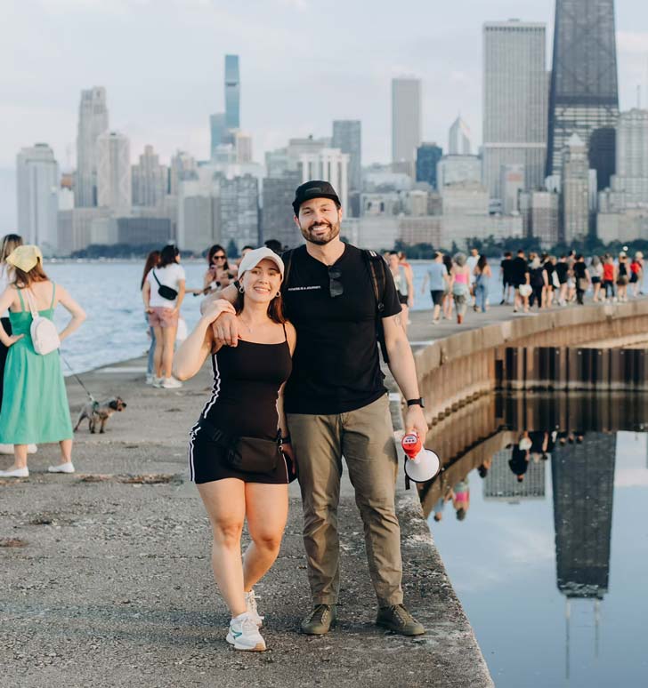 A man and a woman stand on a Chicago pier overlooking Lake Michigan, smiling