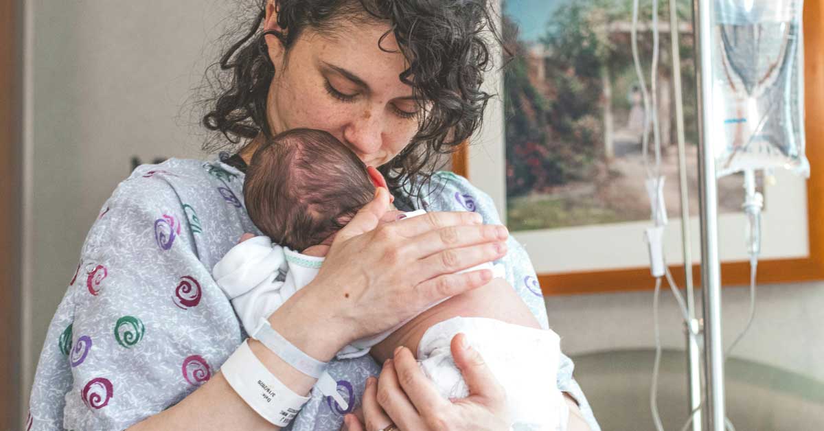 A new mom holds her newborn baby in a hospital gown