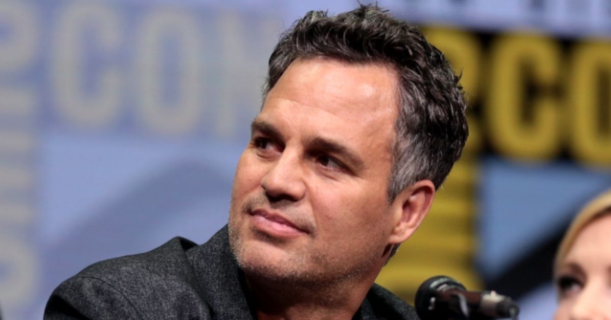 Mark Ruffalo at a Comic Con event sitting at a table in front of a mic
