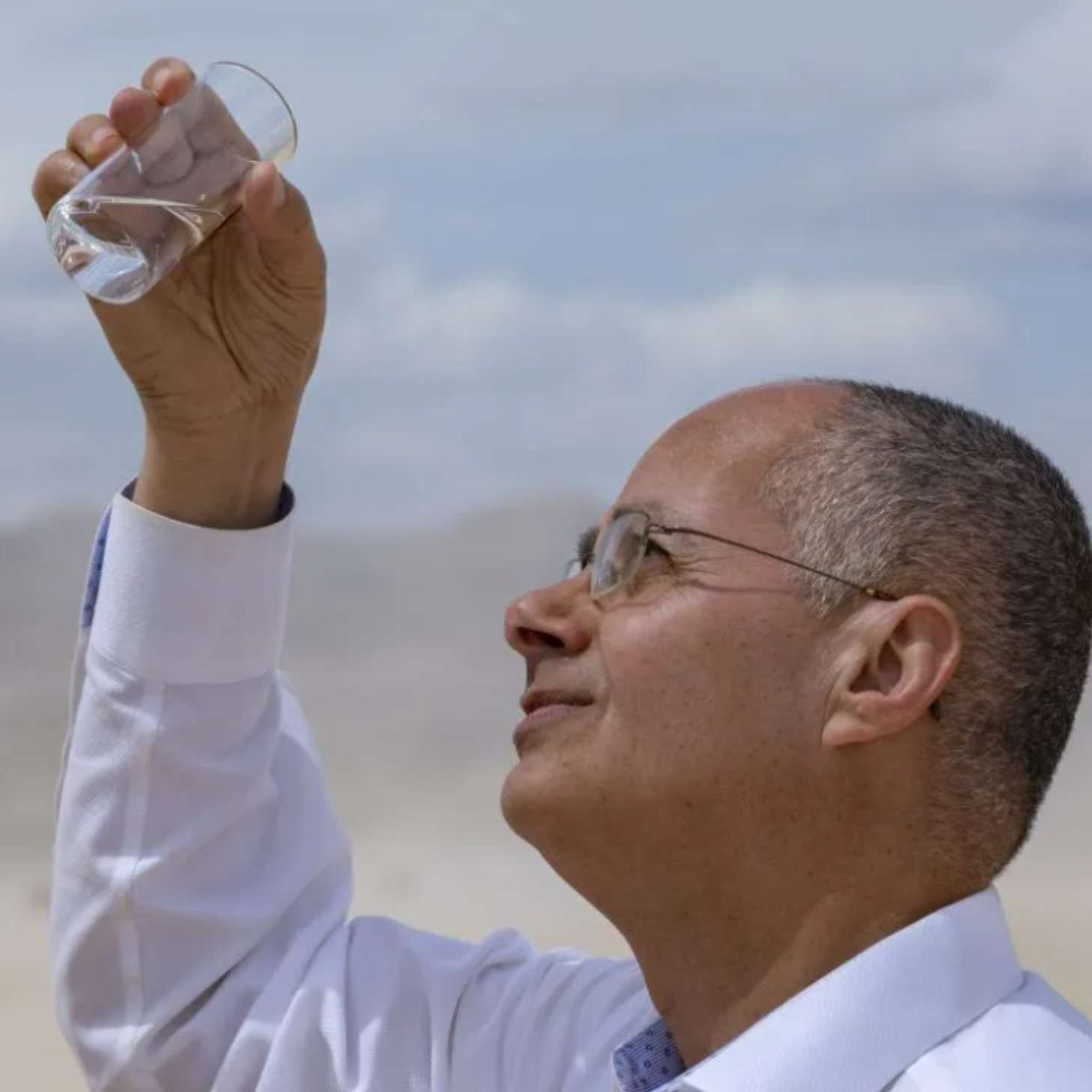 Omar M. Yaghi, an older Jordanian man, holds up a glass of water in the desert.