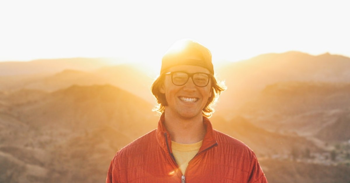 A young man smiles on a mountaintop as the sunsets.