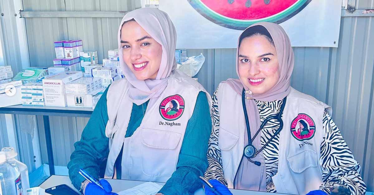 Two young women in hijabs smile outside of a makeshift hospital in Gaza