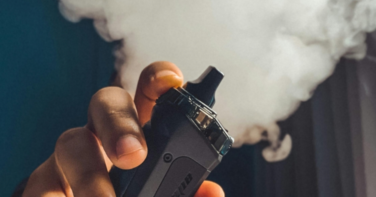 A person holds out a vape, which is emitting a cloud of vapor.