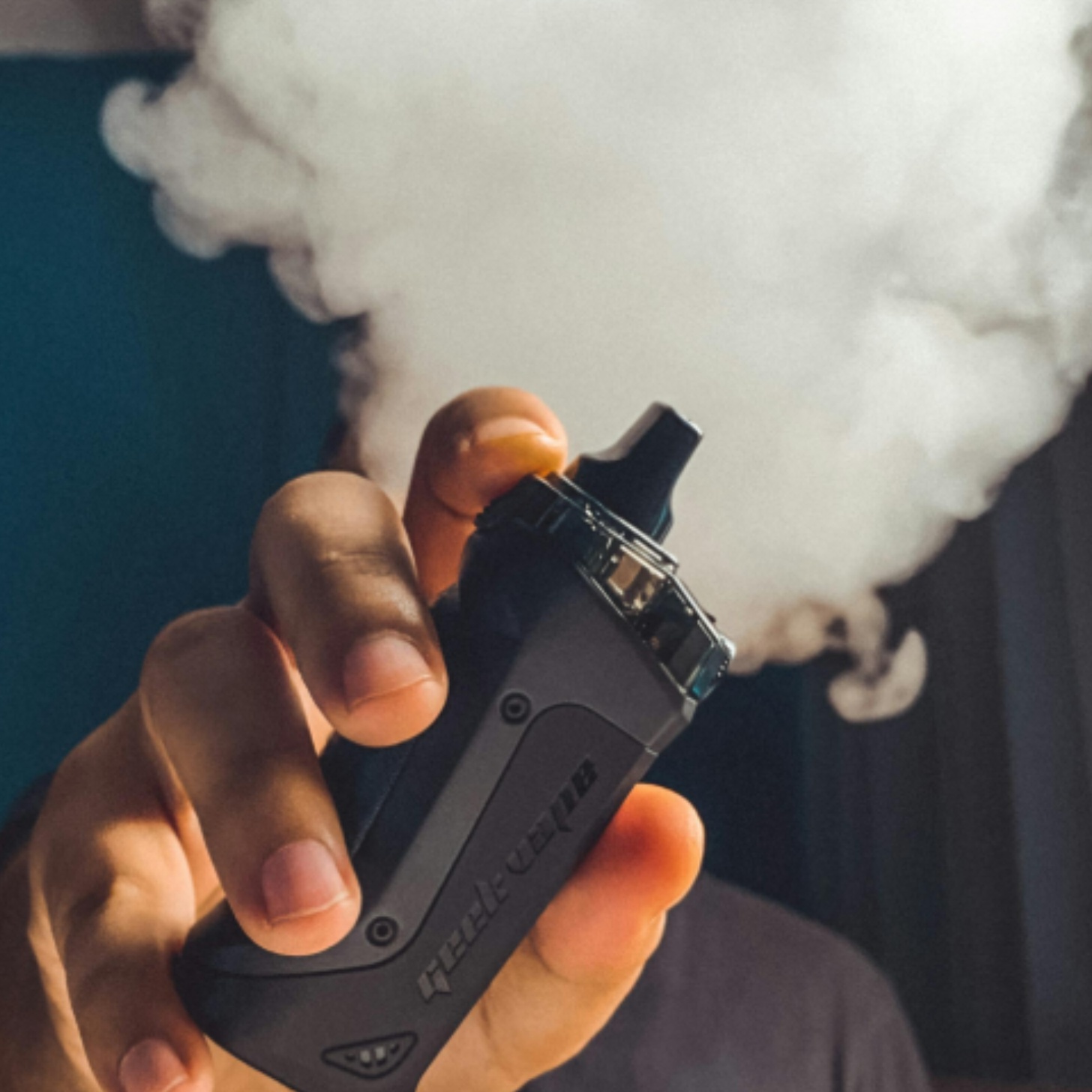 A person holds out a vape, which is emitting a cloud of vapor.