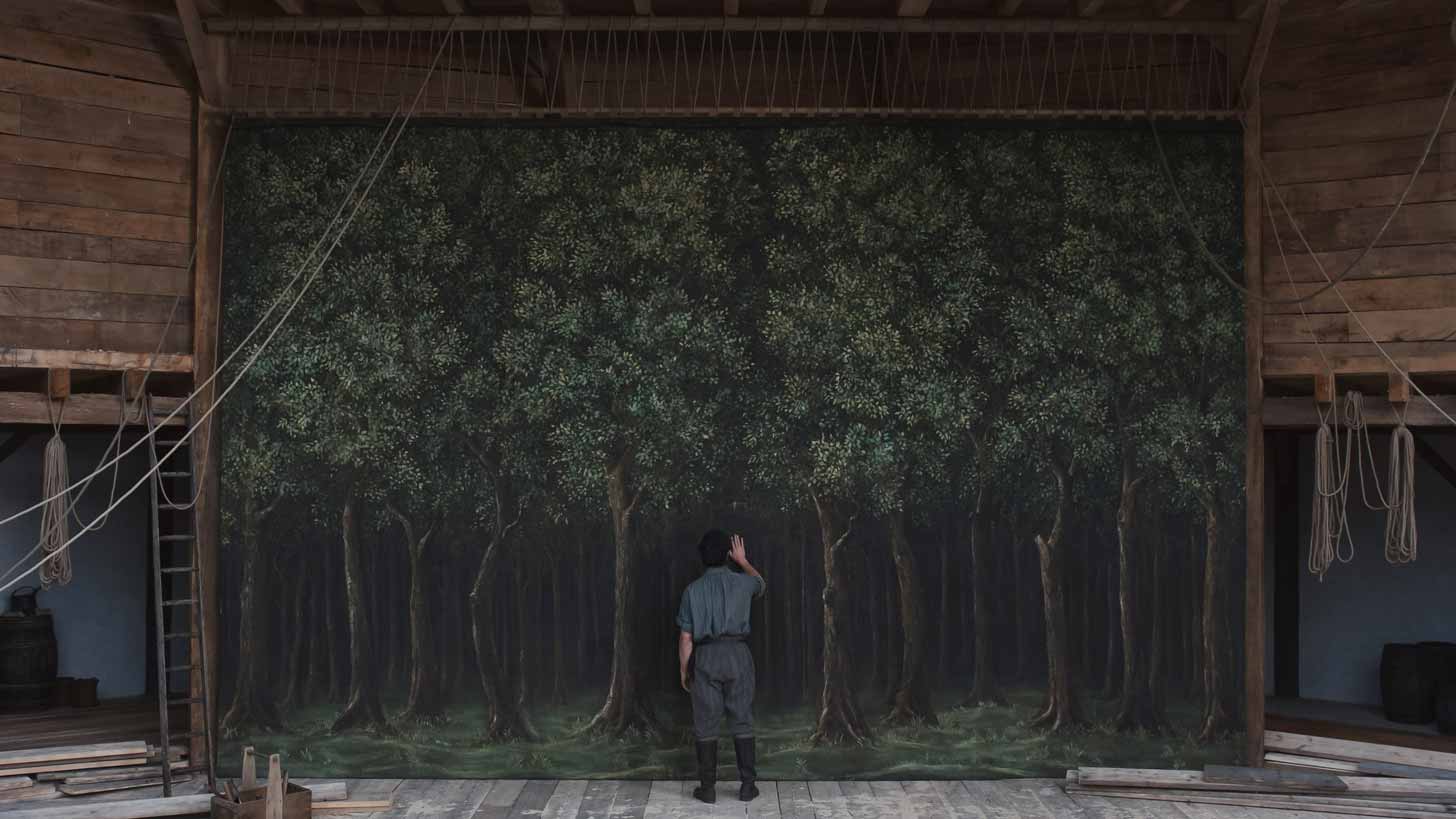Paul Mescal plays William Shakespeare in "Hamnet," standing on a wooden stage and facing a painted backdrop of trees