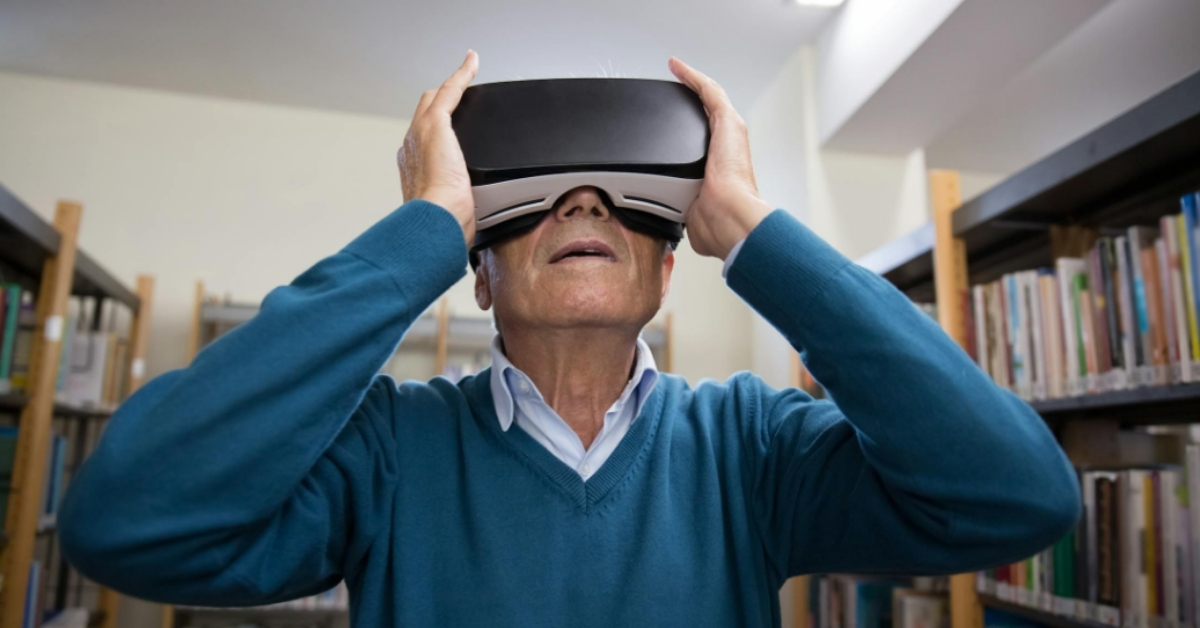 An elderly white man looks through VR goggles in a library.
