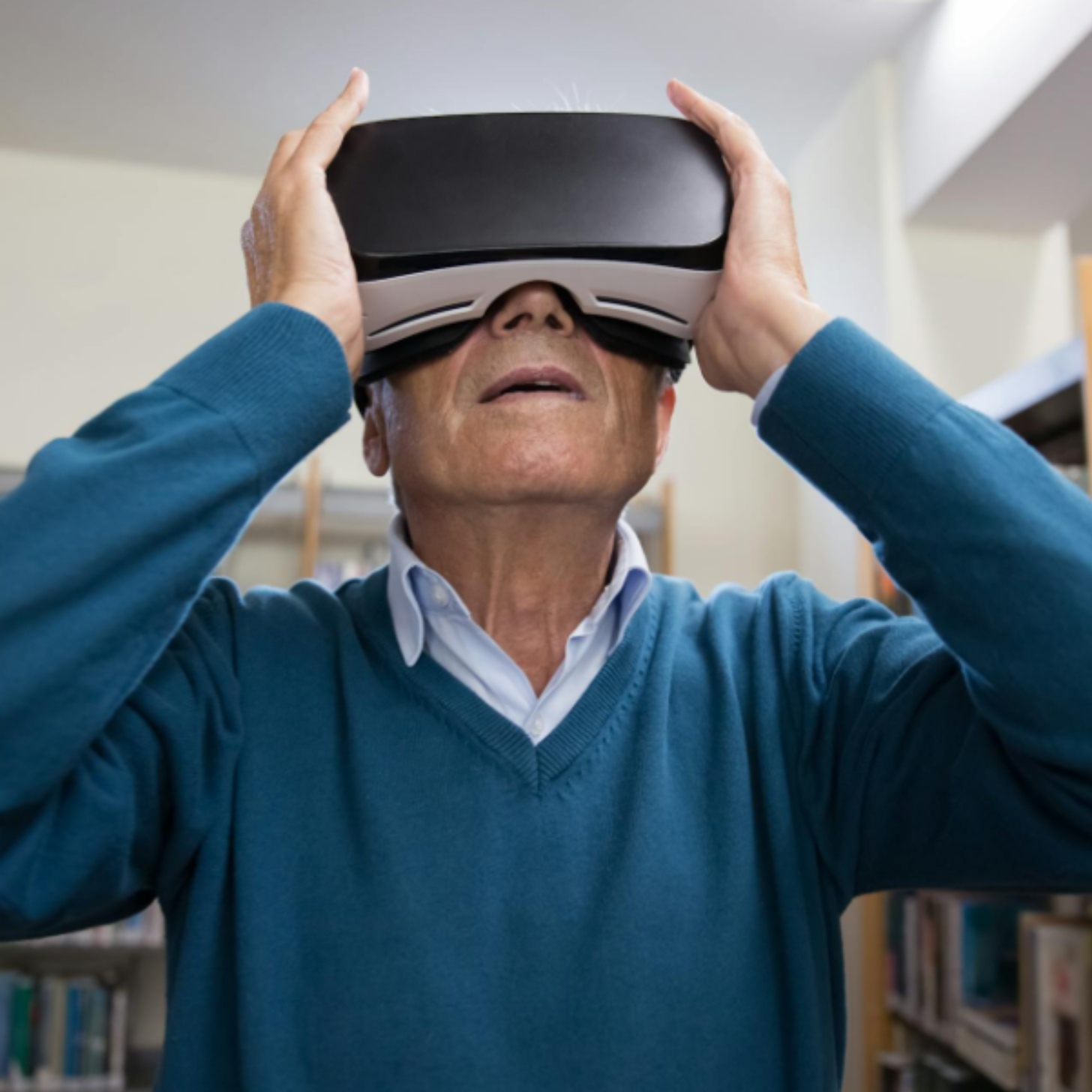 An elderly white man looks through VR goggles in a library.