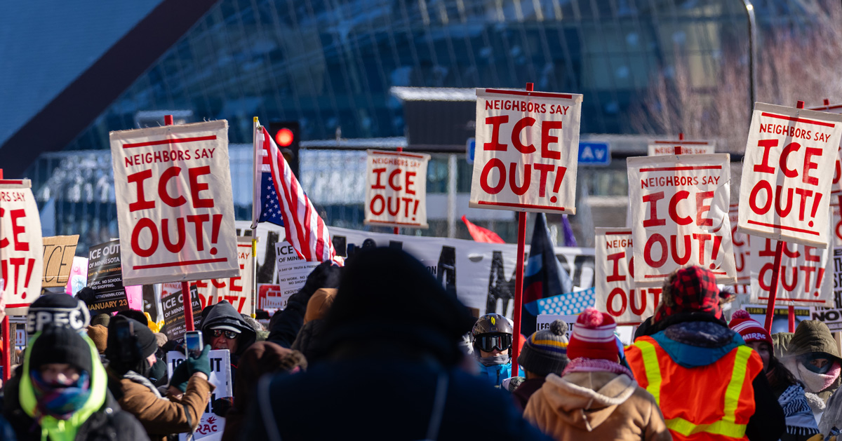 A group of people protesting in the Twin Cities holds up white signs with red letters reading: "Neighbors say ICE OUT"