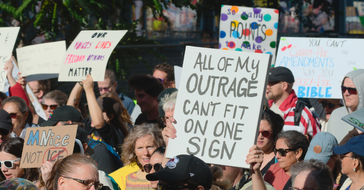 A person holds up a protest sign that reads, "all of my outrage can't fit on one sign."