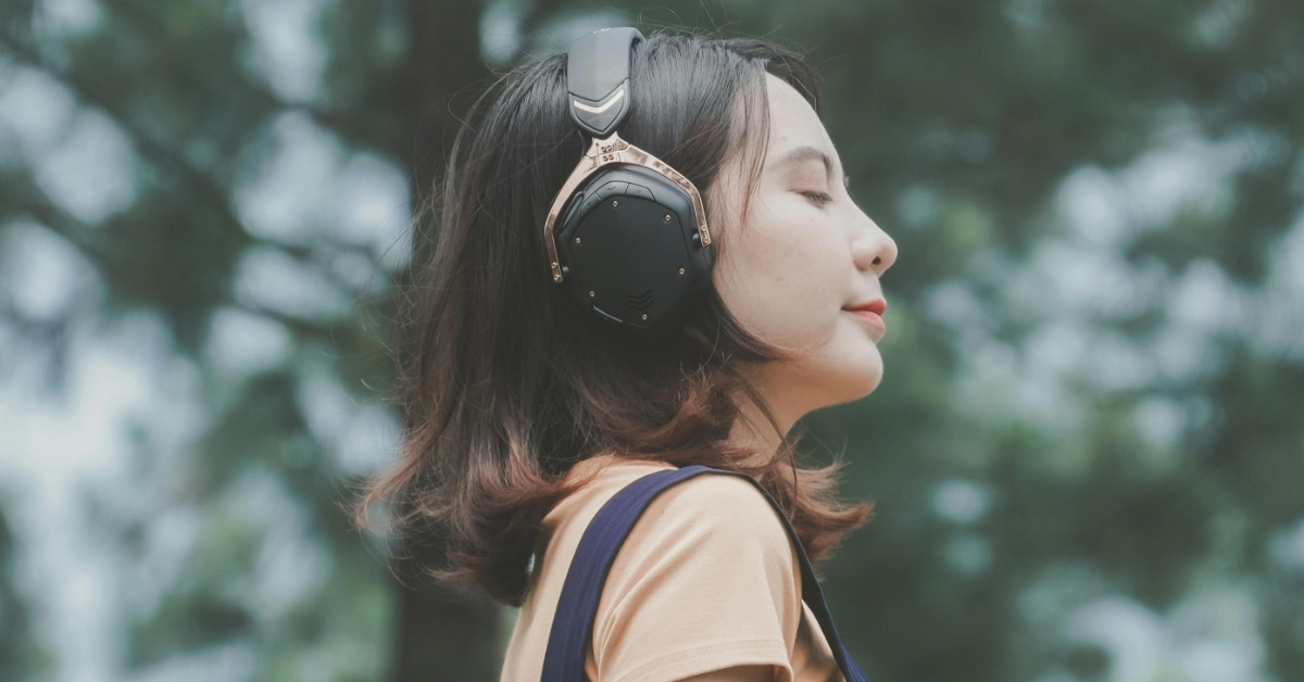 A young woman listens to music on her headphones outside as she smiles slightly, her eyes closed.