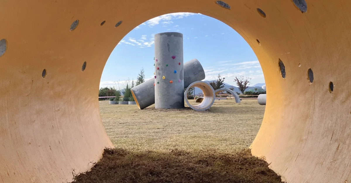 From the perspective of inside of a concrete tunnel, a view of a playground made with recycled cement features
