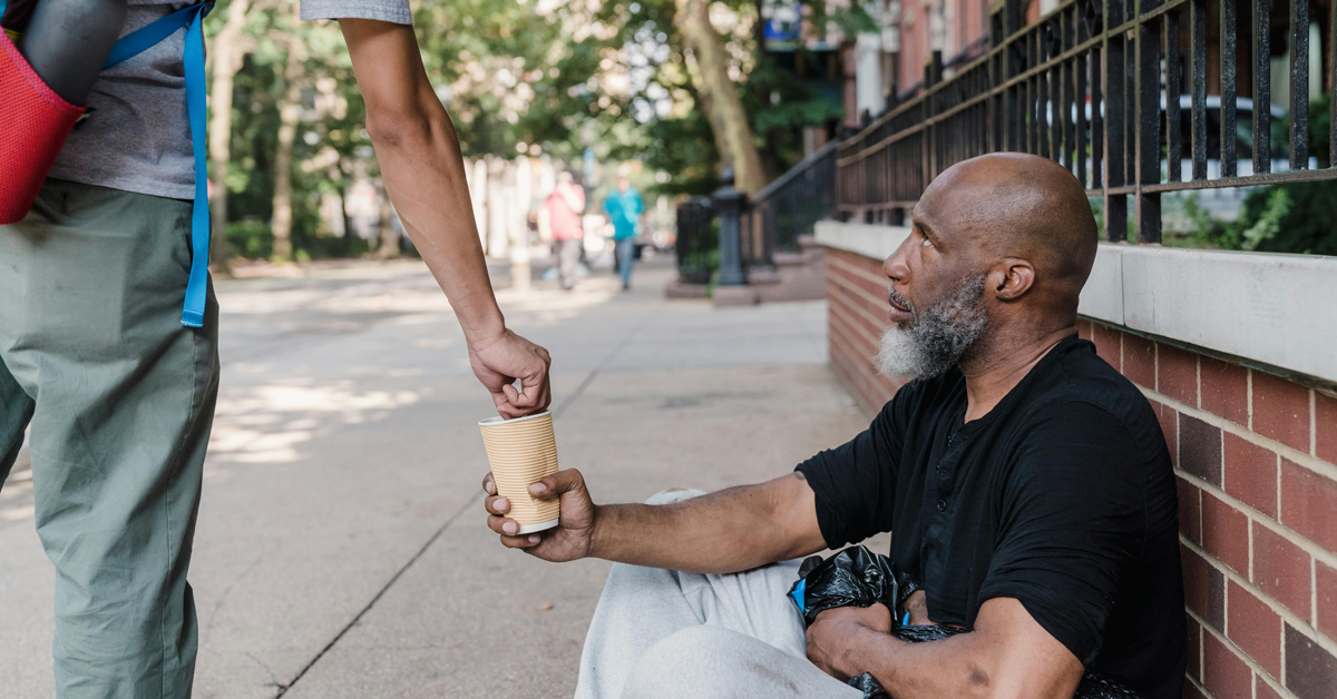 A homeless man reaches out a cup to collect change from a stranger