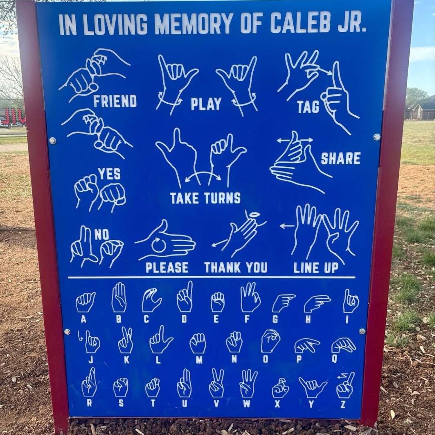 A blue playground sign with white lettering. It has assorted hand signs on it like "tag" "play" "share" etc
