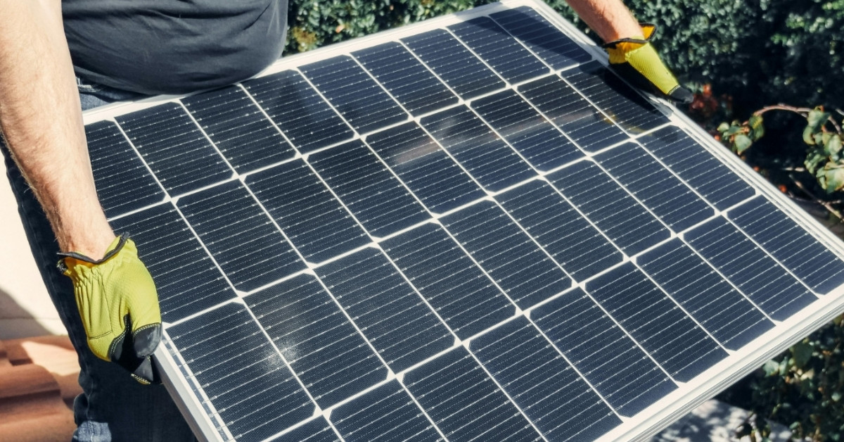 A man with gloved hands holds up a solar panel
