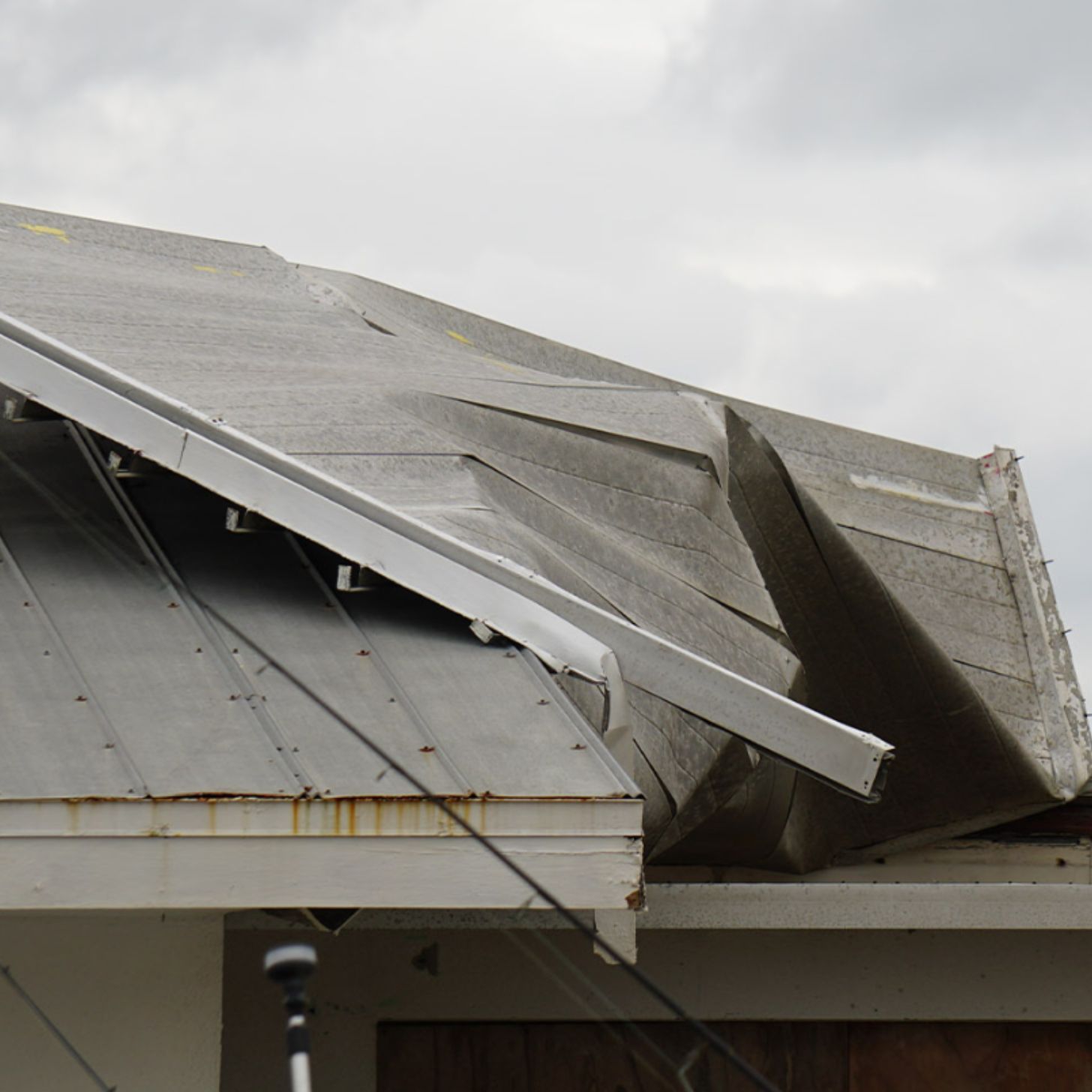 A house roof partially ripped off, under a backdrop of stormy weather,