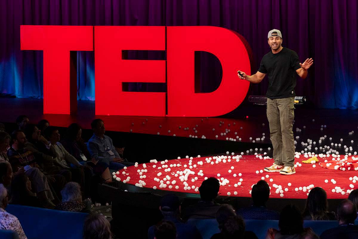 Mark Rober speaks on the TED stage, surrounded by ping pong balls