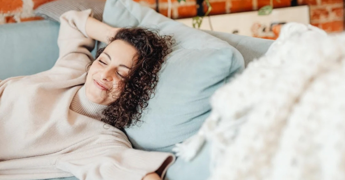 A brunette woman relaxes on a bed while smiling.