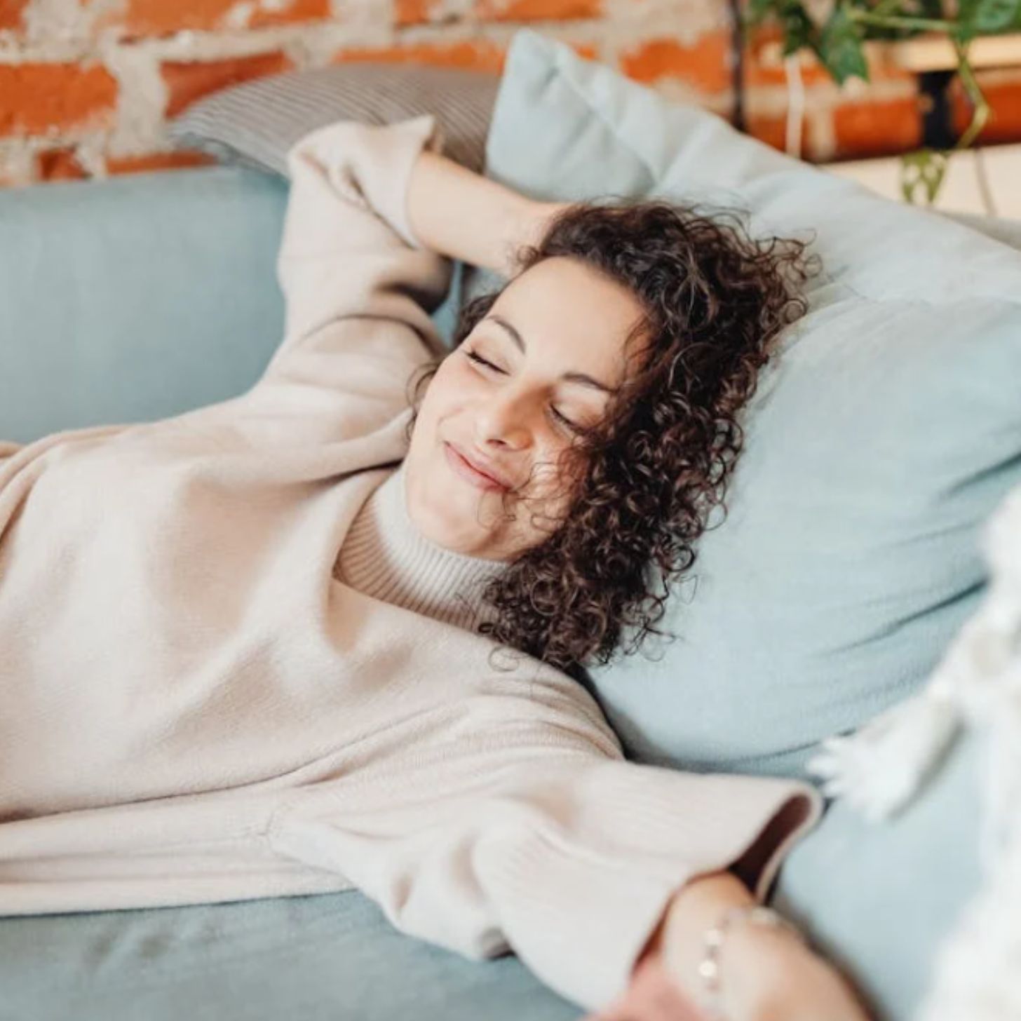 A brunette woman relaxes on a bed while smiling.