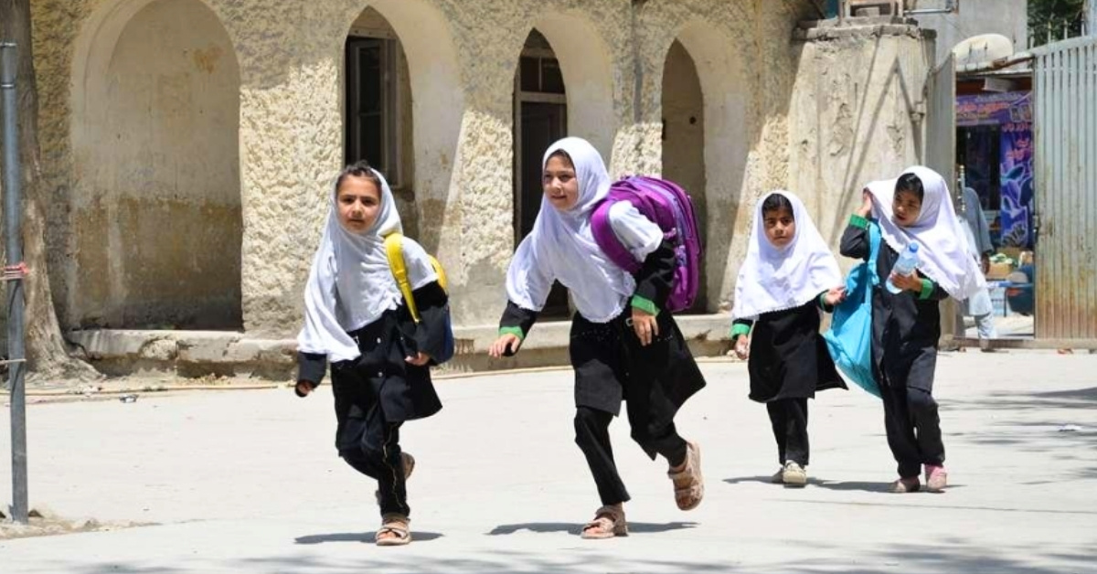 Four little girls run across a cobblestone walkway with backpacks on