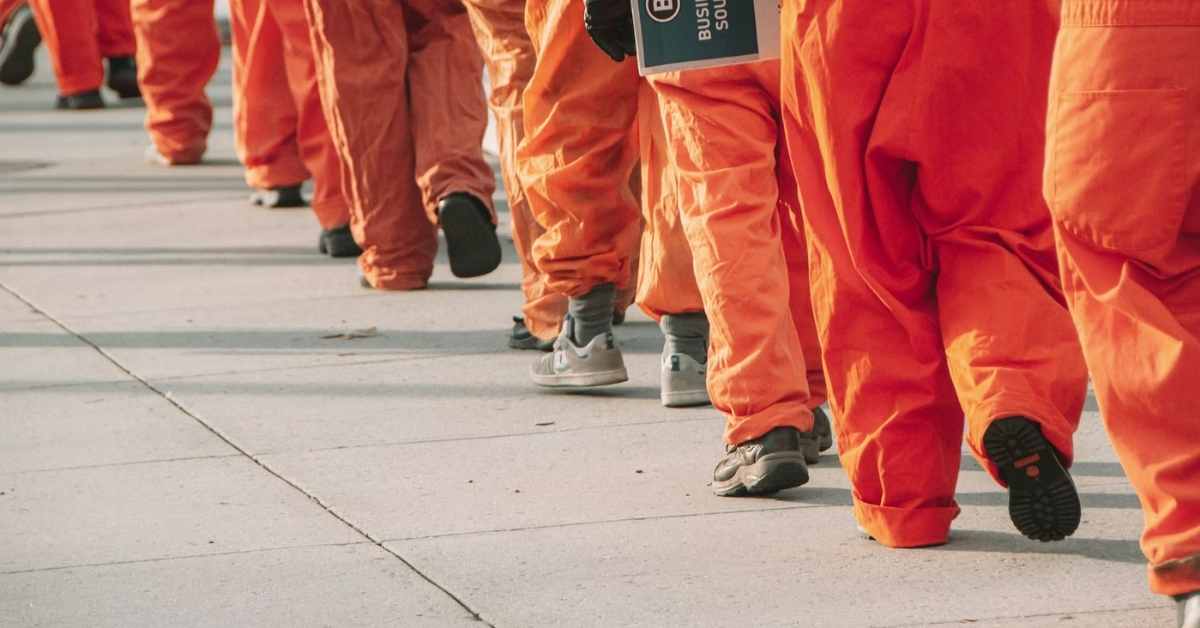 A group of people in orange jumpsuits walking in a line on a sidewalk