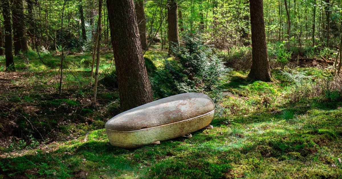 A mushroom casket by Loop Biotech sits in the middle of a lush green forest