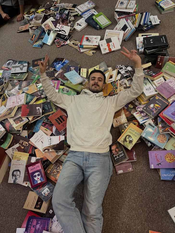 A Palestinian man, Omar Hamad, lays down in a stack of books on the floor of the Phoenix LIbrary