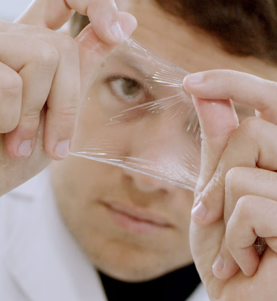 In a closeup, a man in a lab coat inspects a thin layer of seaweed that was made to resemble plastic coating