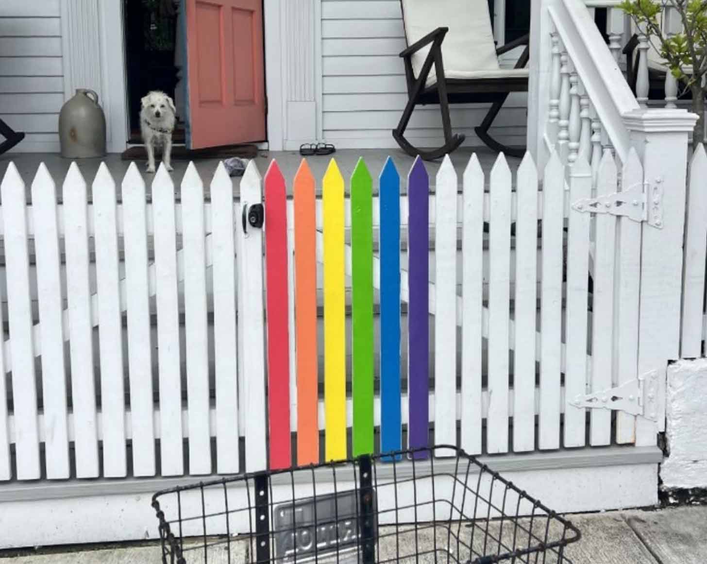 A white picket fence with six panels painted in rainbow colors