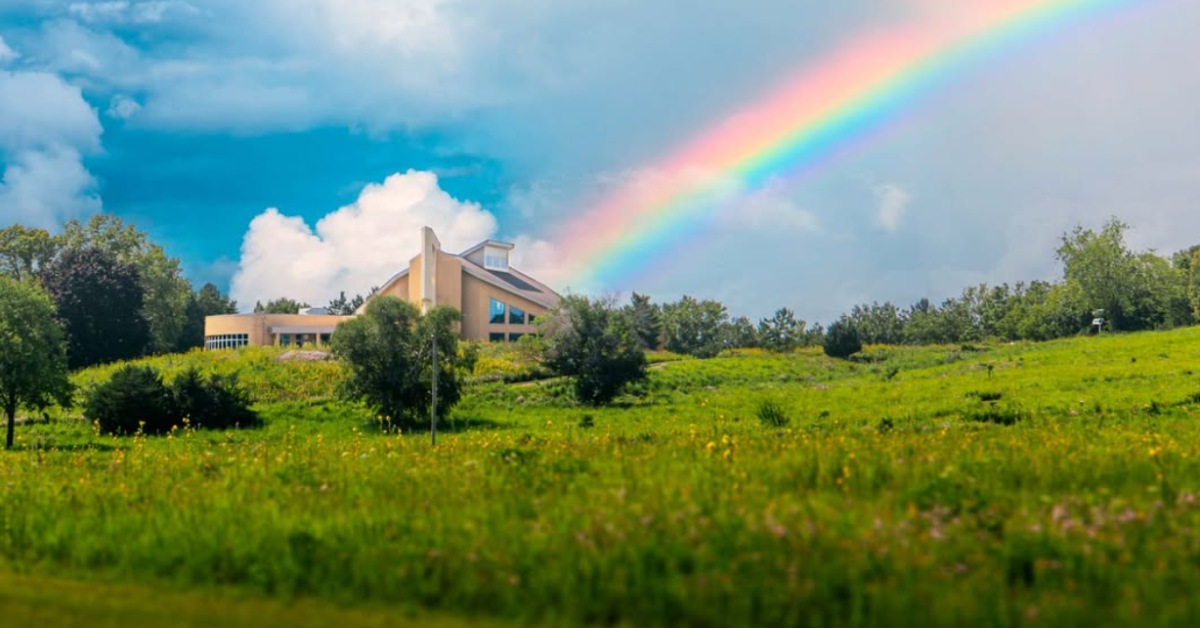 A monastery in a green field with a rainbow shining through the sky