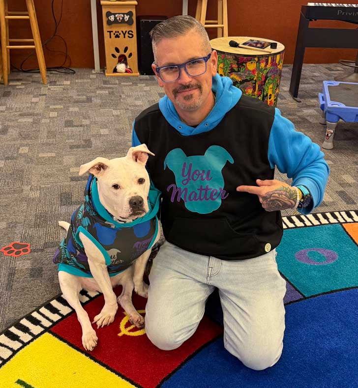 A white pitbull sits with his owner in a music class