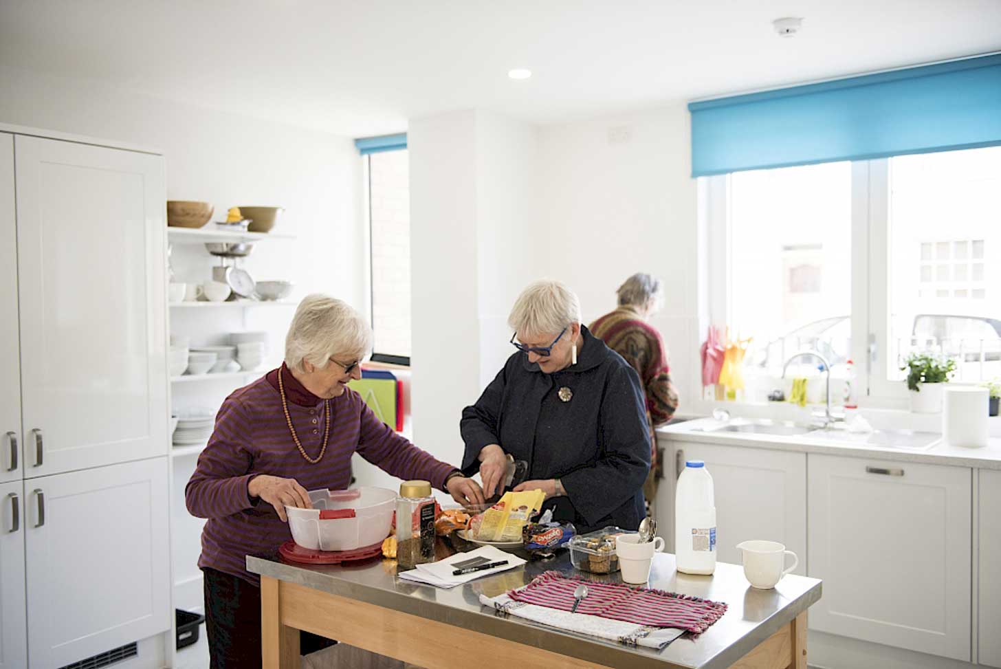 Three elderly women work together in a kitchen