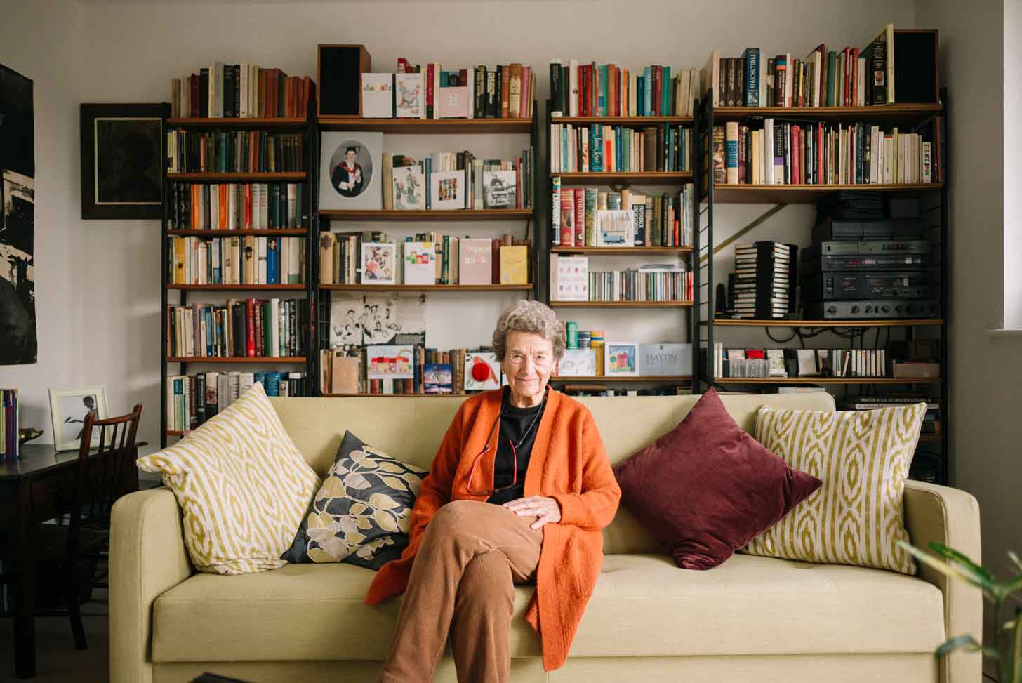 A portrait of an old woman sitting in front of a colorful bookshelf