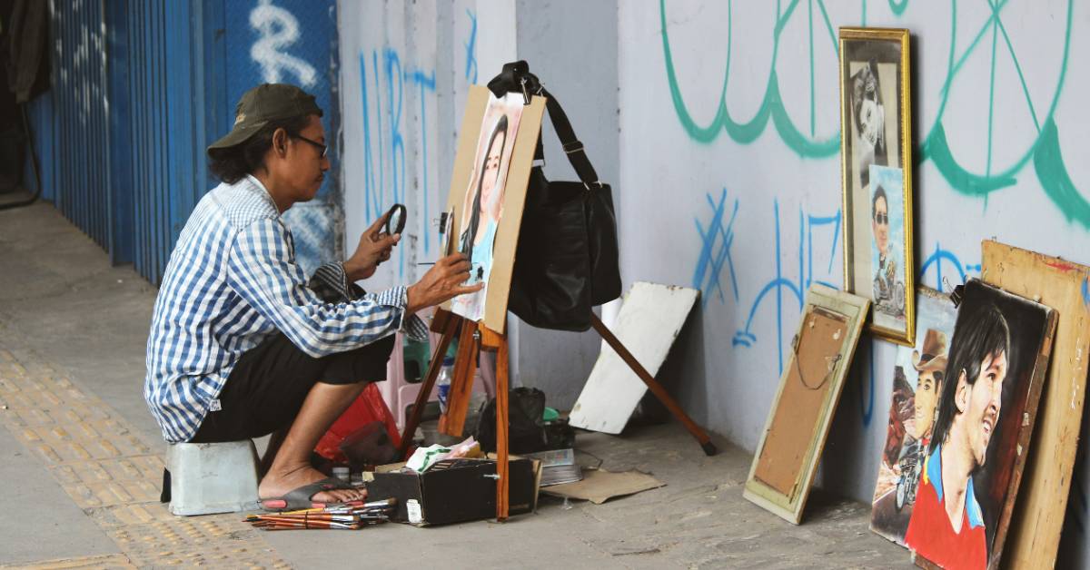 A man paints on a small easel on the streets of a city