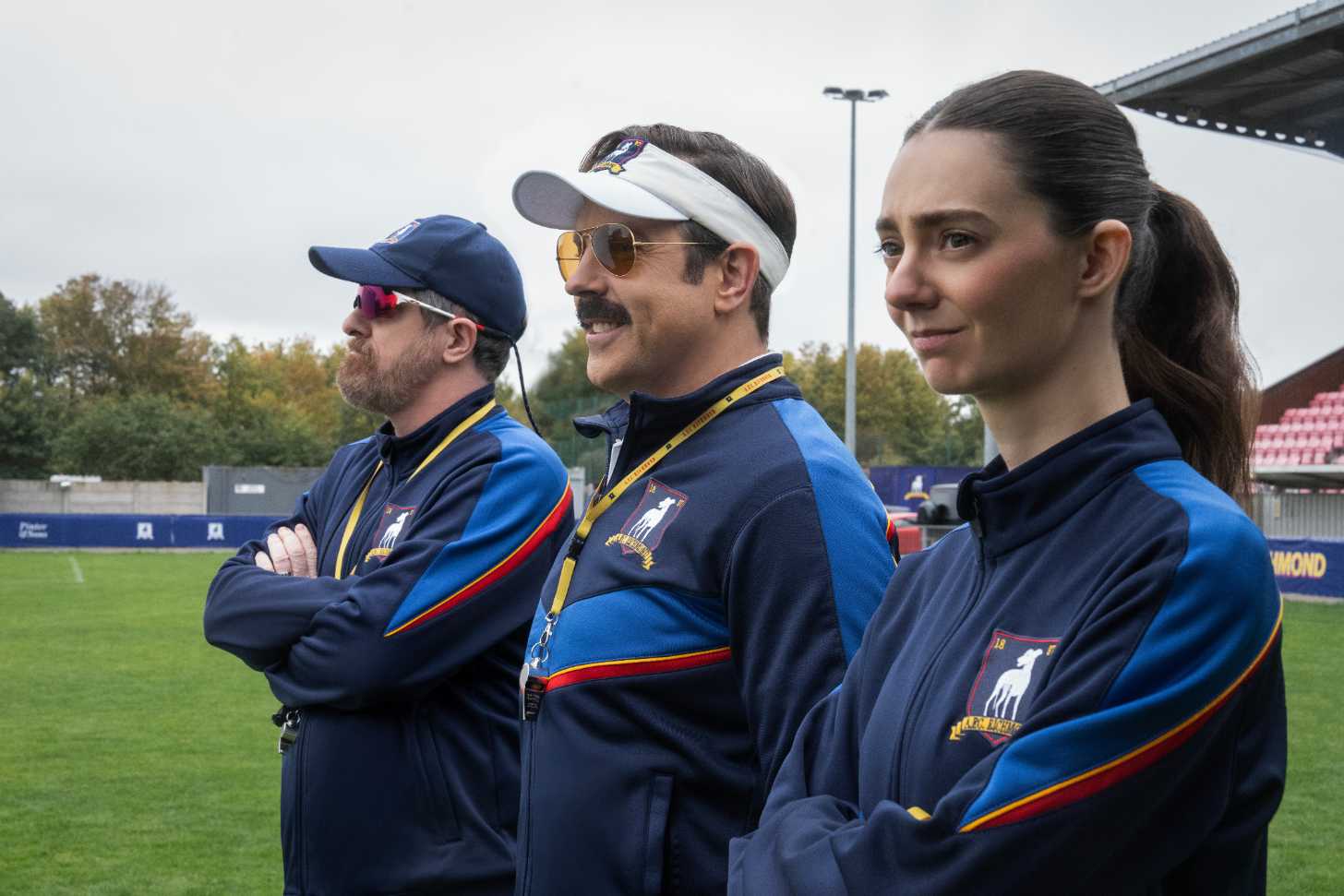 A still from season four of Ted Lasso, with three soccer coaches smiling into the distance