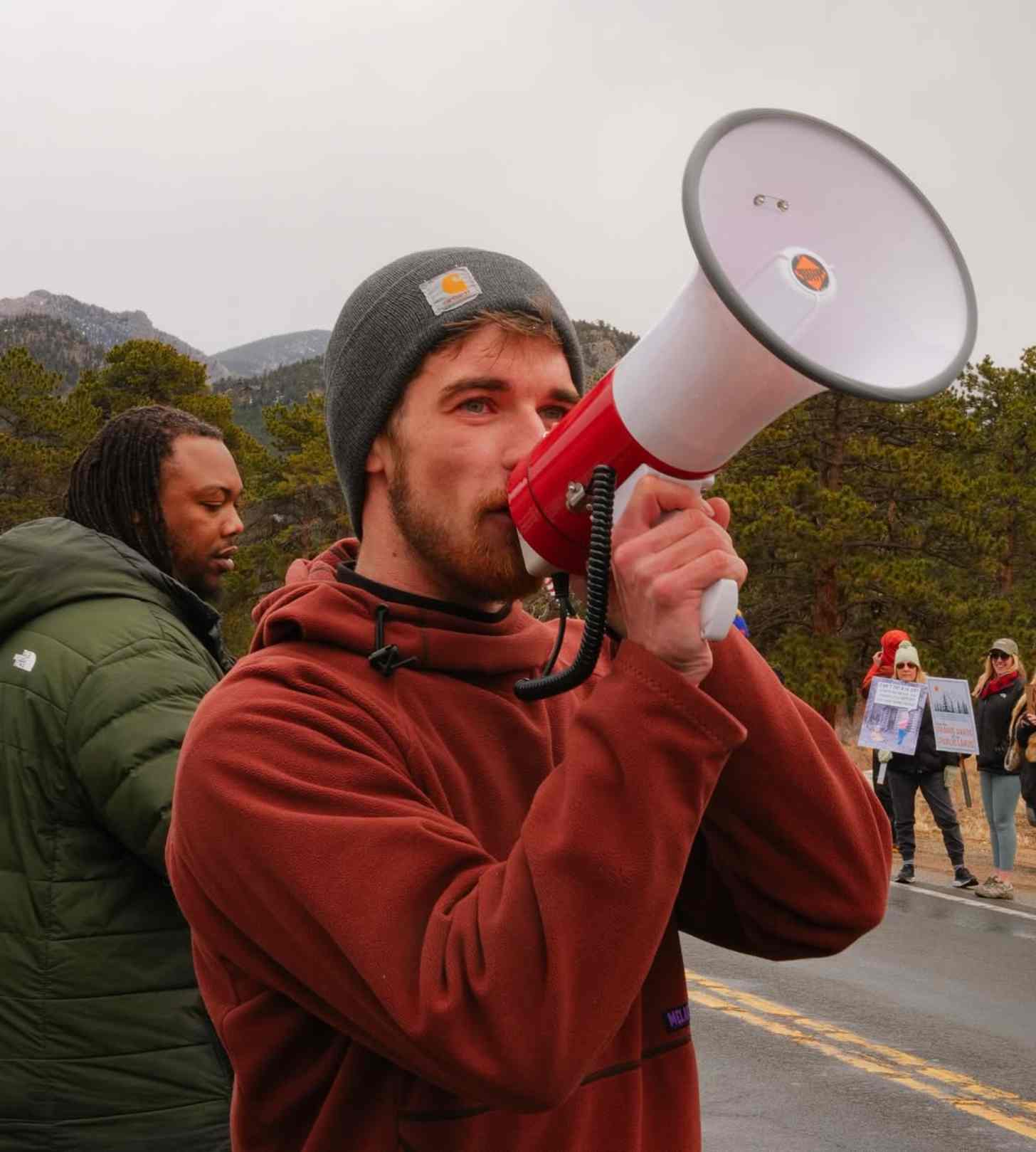 Alex Haraus, a young white man in a Carhartt beanie, speaks into a microphone