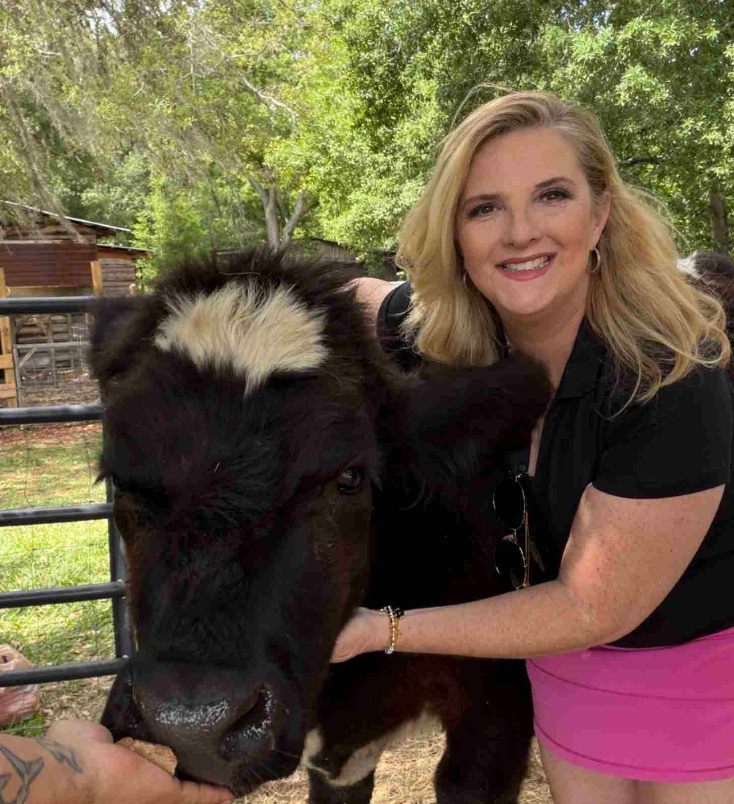 A middle-aged blonde woman smiles beside Charley, a fluffy year old black and white cow