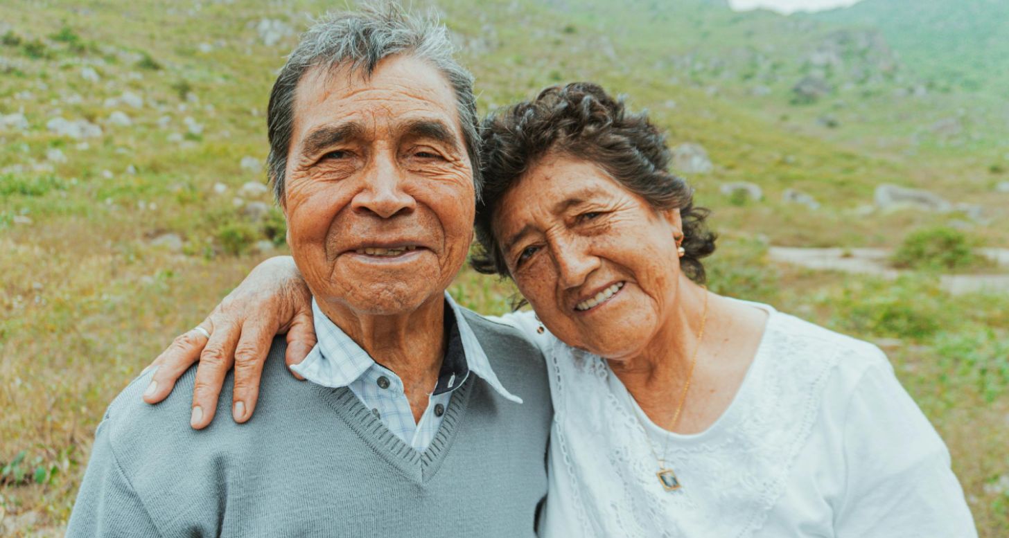 A smiling man and woman, both elderly, in a field
