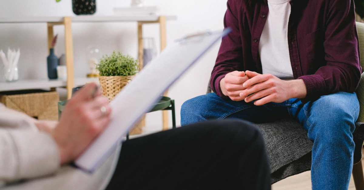 A man sits with his hands folded in his lap in a therapy office