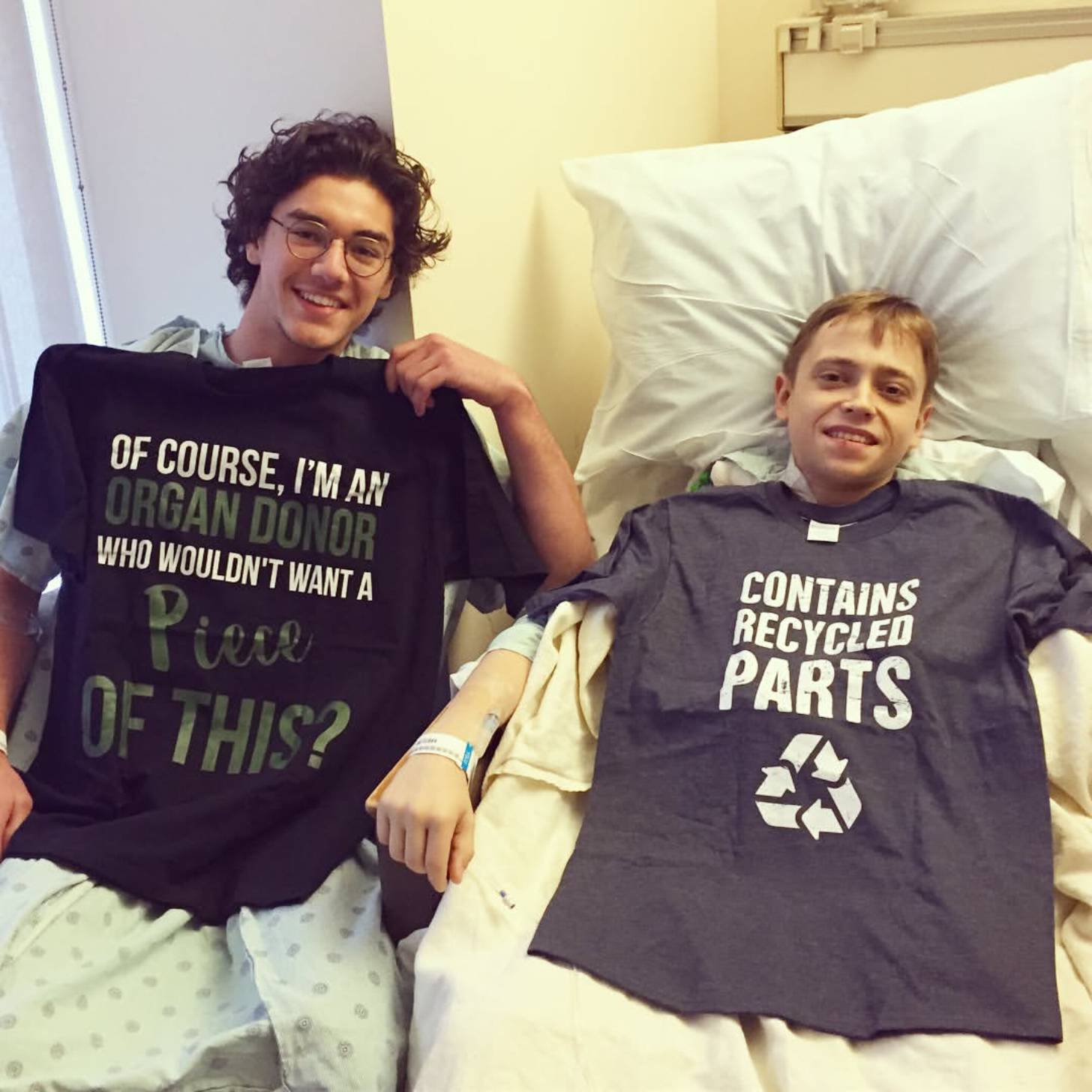 Actor Belmont Cameli smiles next to a patient in a hospital bed